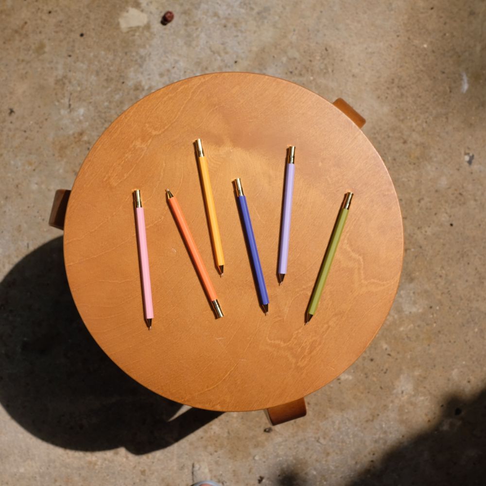 Colorful markers on a round wooden stool against a concrete floor.
