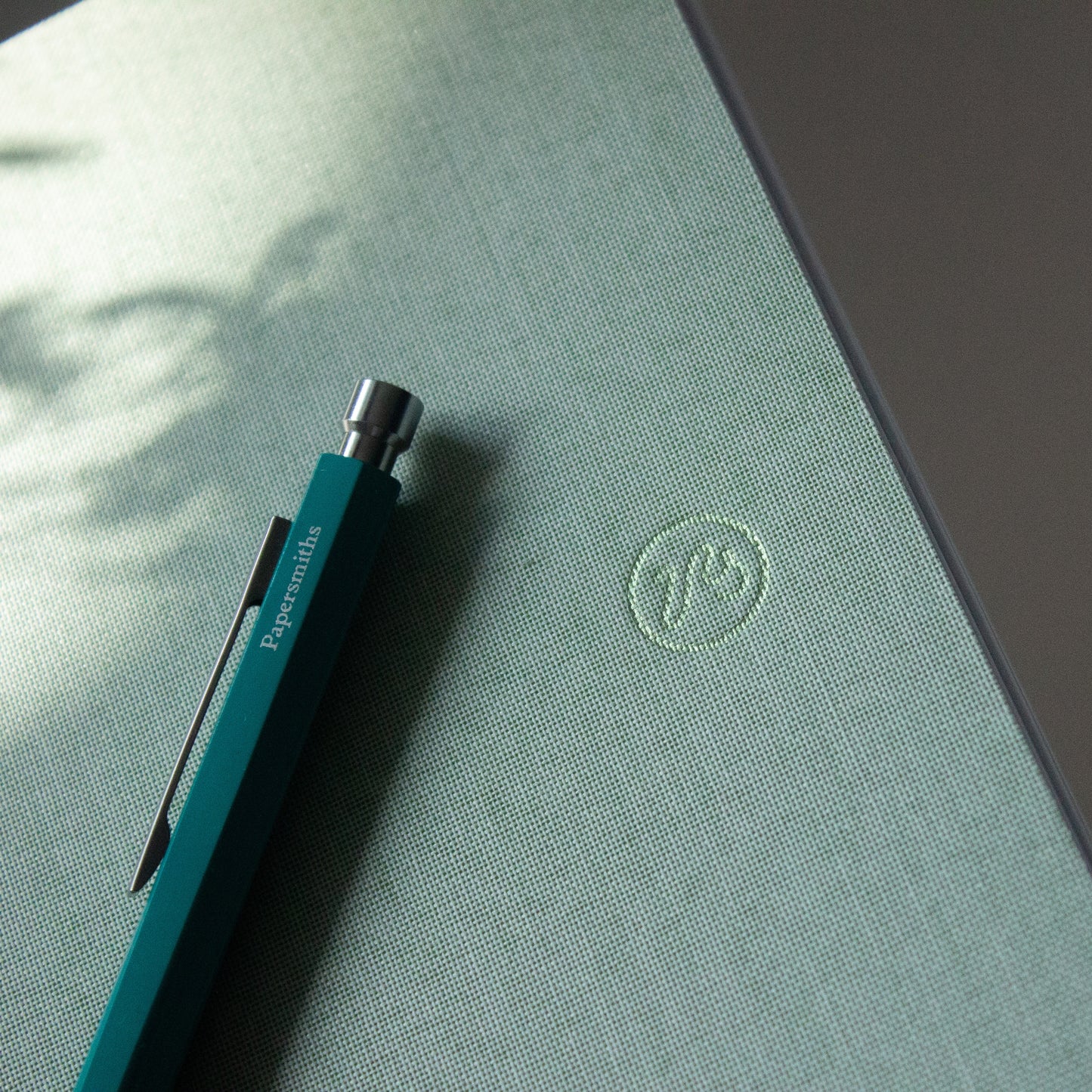 Blue pen on a green surface with a logo, on a blurred natural background